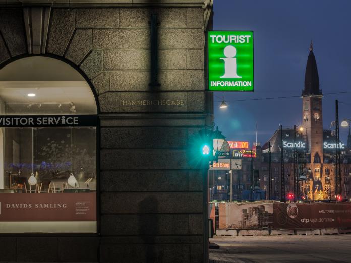 Copenhagen Visitor Service by night med et lysende grønt turistskilt med et stort hvidt I